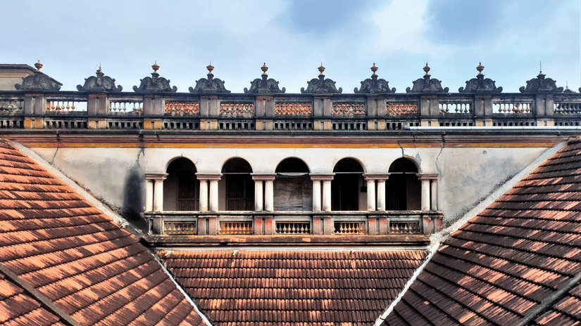 A view of a traditional building with orange clay tile roofs, a white balcony with arched pillars, and ornate stone railings.