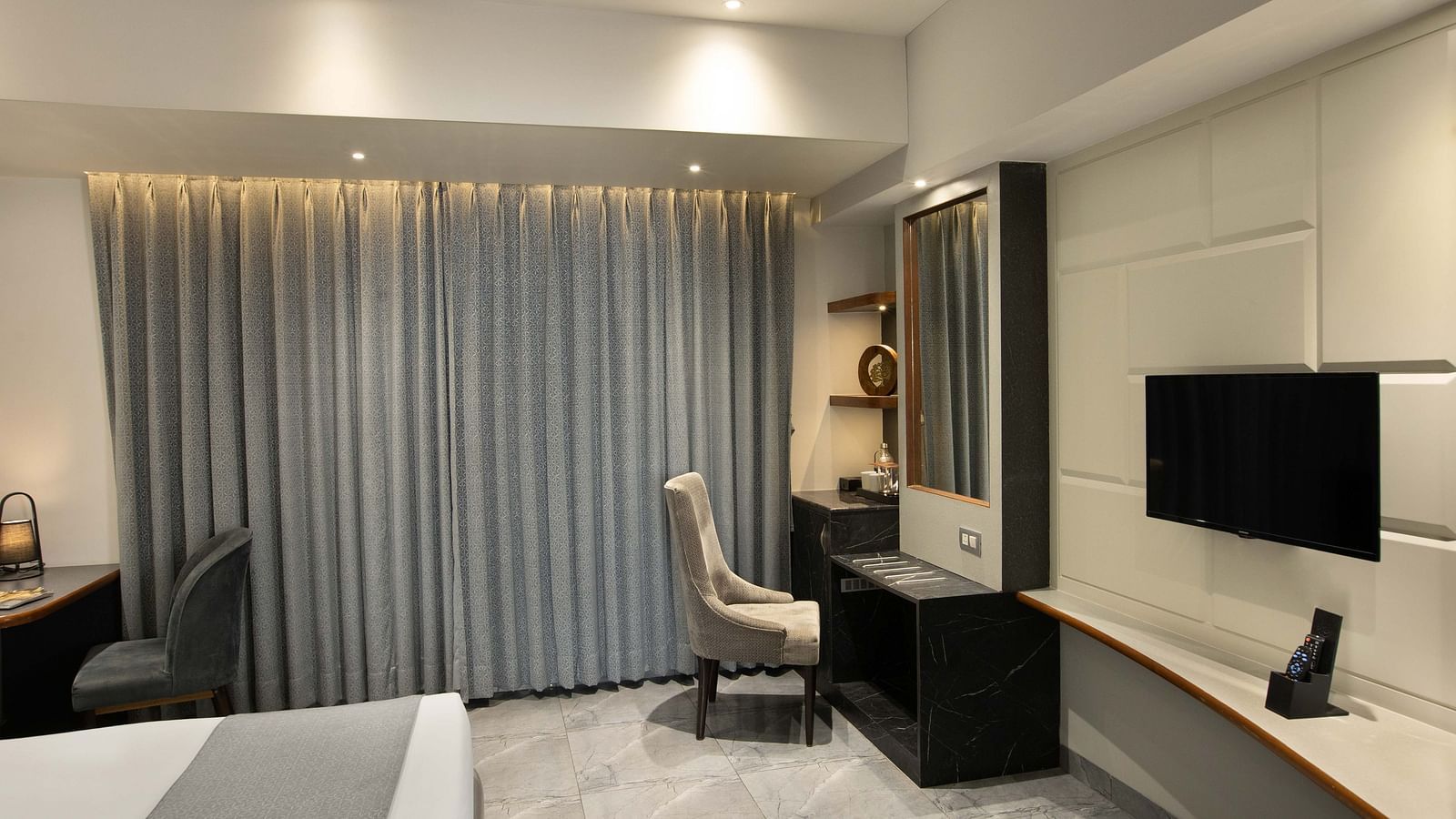 Image of the Coral Deluxe Room at Coral Reef Hotel & Spa in Port Blair featuring chair in front of the mirror next to the window and a TV mounted on the wall in front of the bed