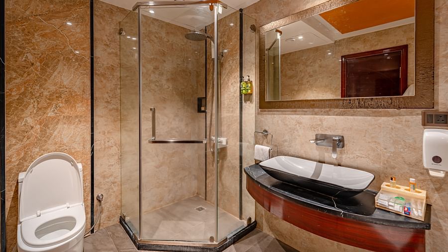 Executive Suite bathroom features a wall-mounted hand wash, hairdryer, a horizontally placed mirror above the wash basin, and a western toilet seat at Crescent Spa & Resort, Indore