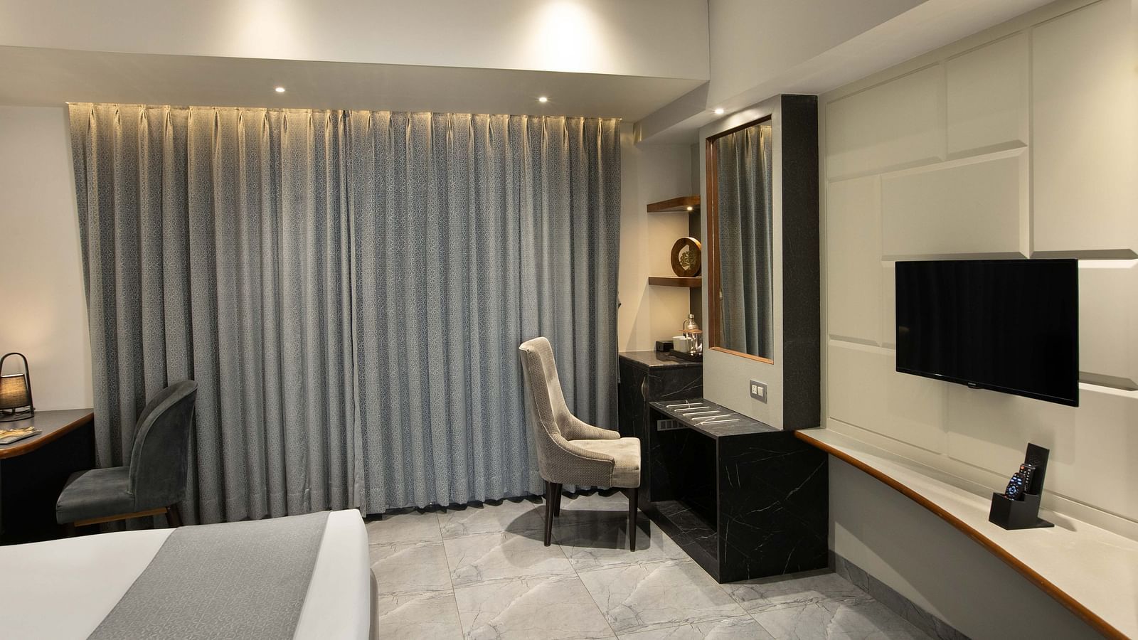 Image of the Coral Deluxe Room at Coral Reef Hotel & Spa in Port Blair featuring chair in front of the mirror next to the window and a TV mounted on the wall in front of the bed