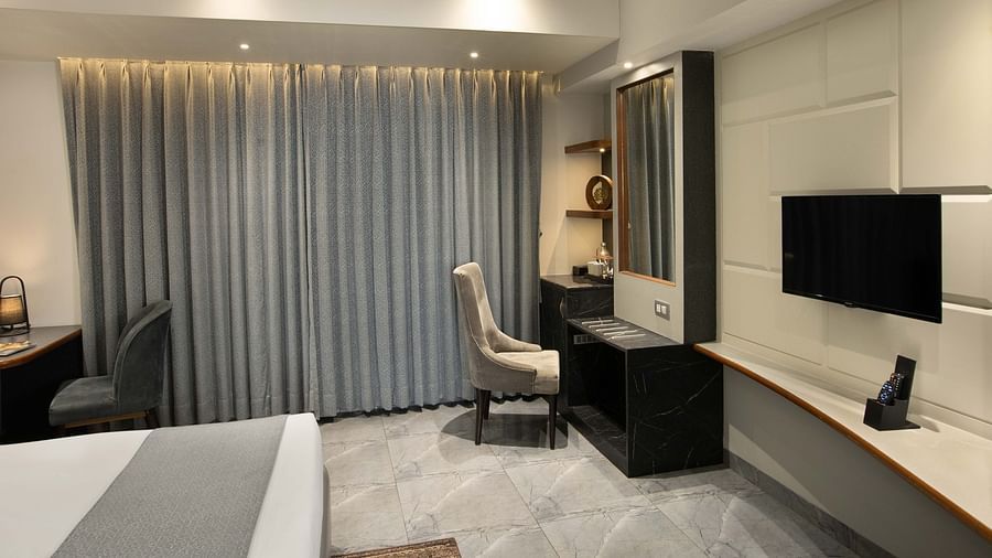 Image of the Coral Deluxe Room at Coral Reef Hotel & Spa in Port Blair featuring chair in front of the mirror next to the window and a TV mounted on the wall in front of the bed