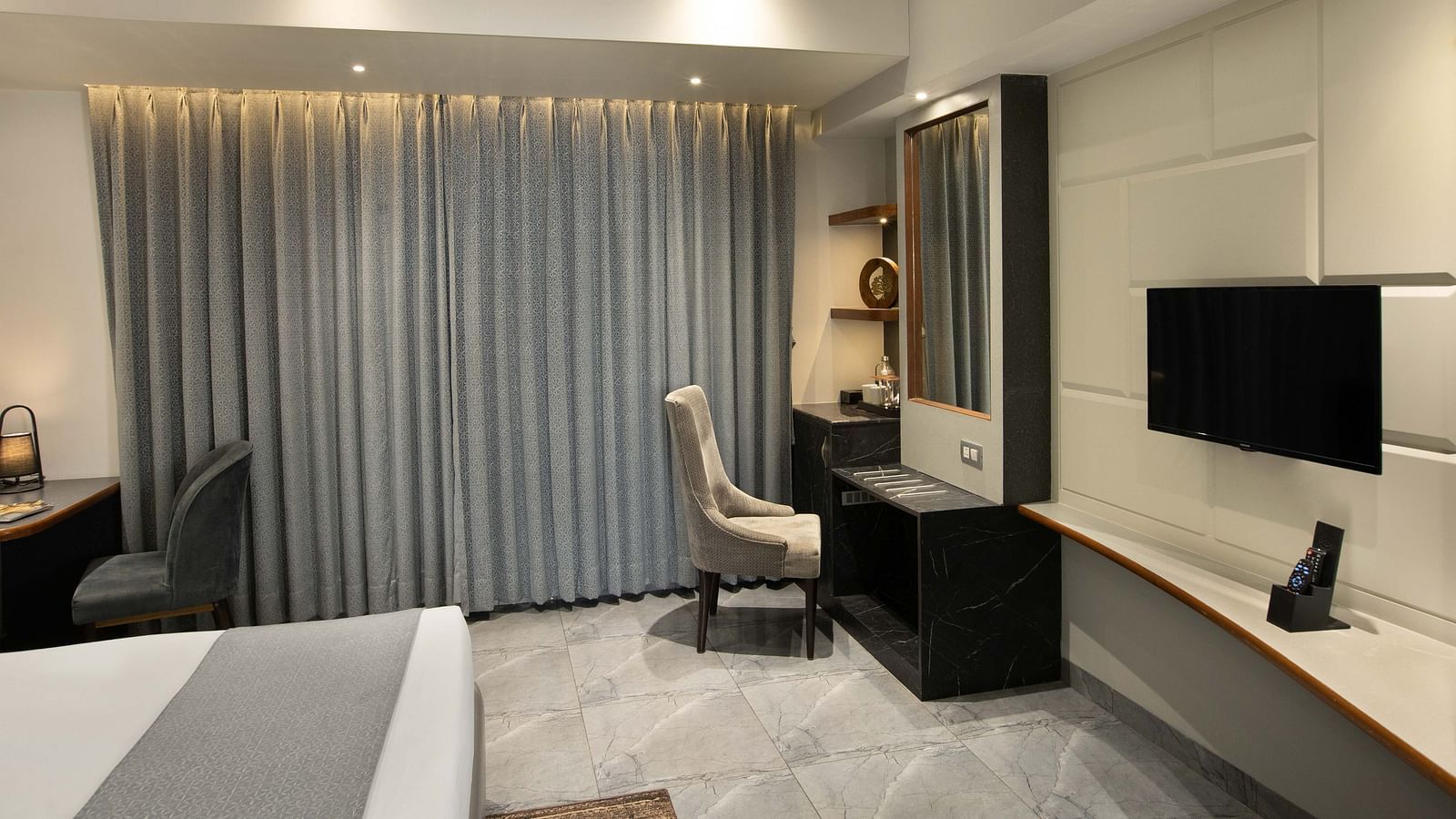 Image of the Coral Deluxe Room at Coral Reef Hotel & Spa in Port Blair featuring chair in front of the mirror next to the window and a TV mounted on the wall in front of the bed