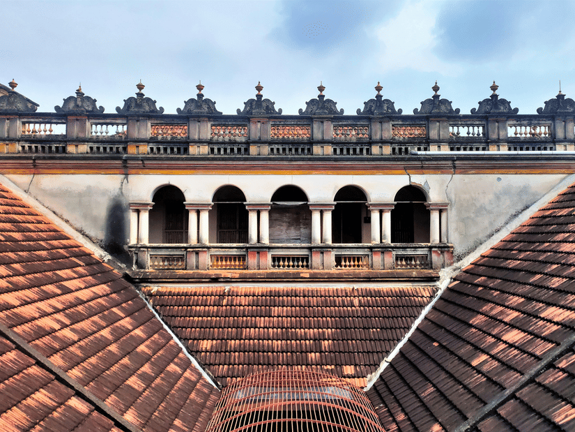 Traditional Chettinad mansion rooftop with terracotta tiles, elegant arches, and an upper balcony showcasing the grandeur of heritage architecture.