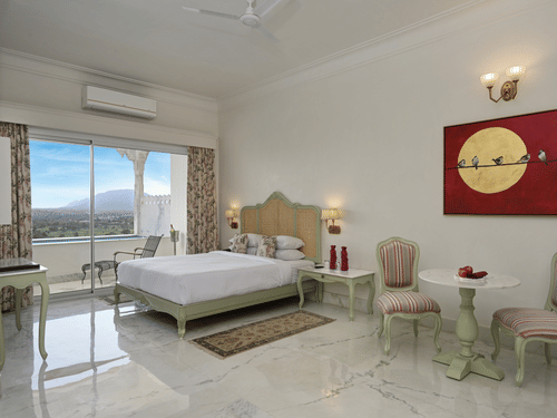 A well-lit Plunge Pool Suite at Khas Mahal Suites, Udaipur featuring a bed, seating area, and a large window with a view.