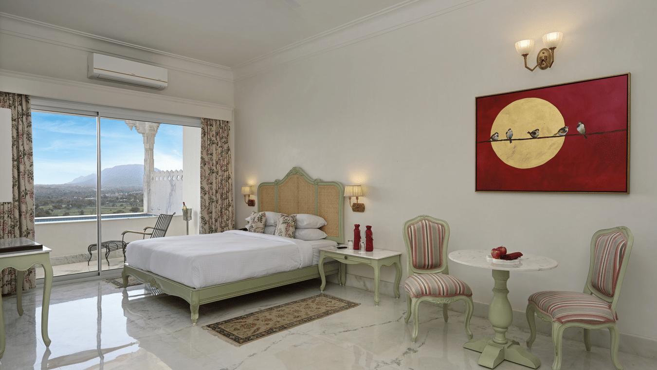 A well-lit Plunge Pool Suite at Khas Mahal Suites, Udaipur featuring a bed, seating area, and a large window with a view.