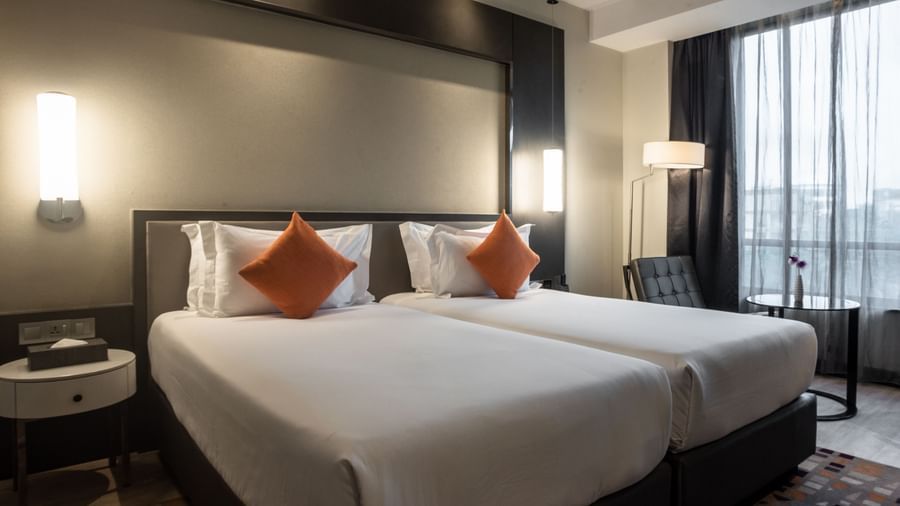 Twin bed hotel room with two beds, orange cushions, bedside tables, and windows at Best Western Premier Westlands.