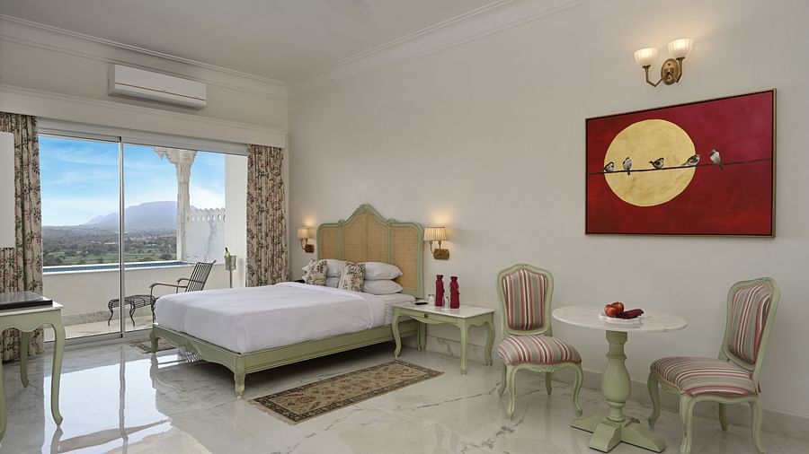 A well-lit Plunge Pool Suite at Khas Mahal by Fateh Collection, Udaipur featuring a bed, seating area, and a large window with a view.