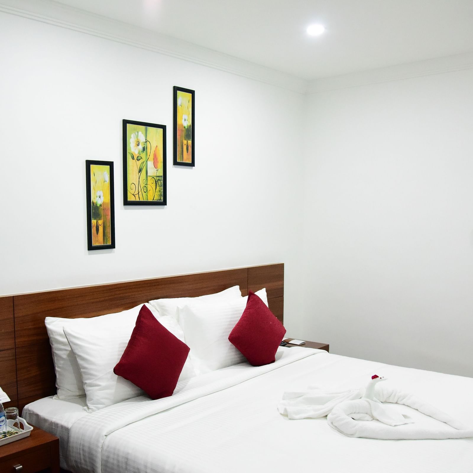 The luxurious comfort club room at The Royal Comfort hotel, featuring a plush bed with white linens and two deep red accent pillows, elegantly decorated walls, and a bedside table with amenities.