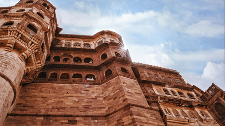 An upward, dramatic view of the immense sandstone walls of Nahargarh Fort in Jodhpur against a bright sky.