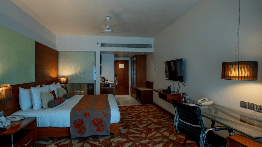 Elegant king bedroom with warm wooden interiors and in-room dining setup at The Pride Premier Nagpur.
