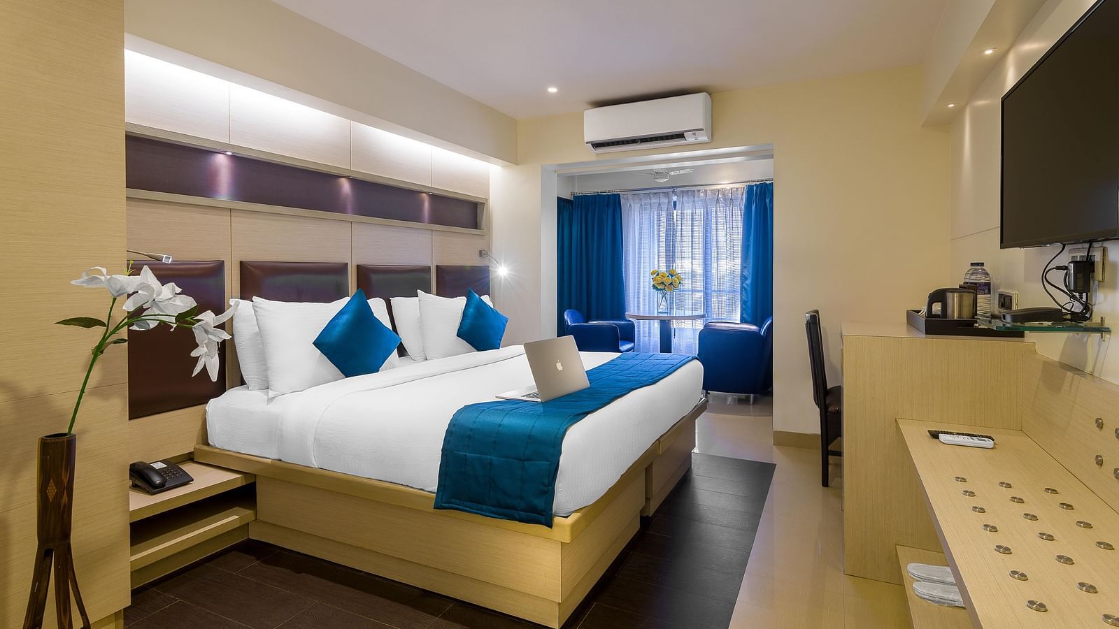 Side view of a spacious room with large bed, pillows, sheets, window with curtains, AC above, and wall-mounted TV at Oriental Aster, Mumbai.