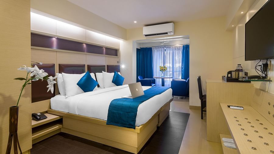 Side view of a spacious room with large bed, pillows, sheets, window with curtains, AC above, and wall-mounted TV at Oriental Aster, Mumbai.