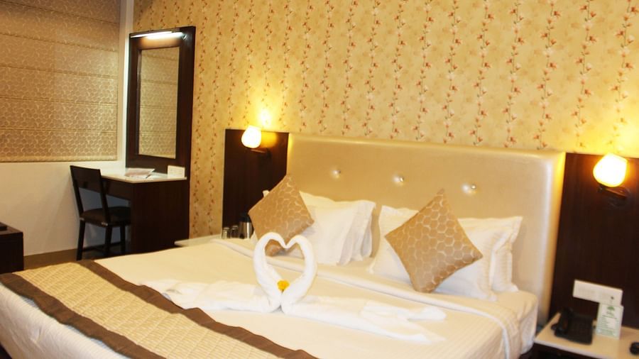 A warmly lit hotel room with a queen size bed, white bedding and a towel art swan on the bedspread - TGI Apple Inn, Jaipur 