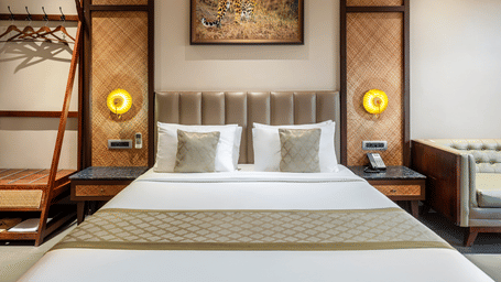 A neatly made double bed is adorned with plush pillows and an elegant patterned runner under a painting - Sajjan Bagh Resort and Spa, Kumbhalgarh