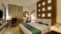 Superior Room at Pride Premier Chennai featuring a plush bed with a fancy headboard and a work desk along with sitting space in the background