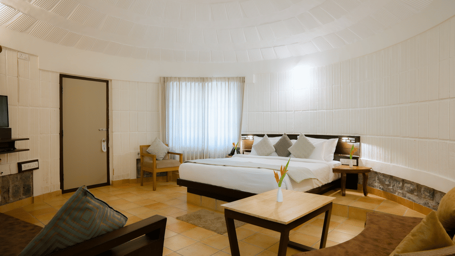 A spacious room featuring a king size bed, coffee table, and sofa unit on tiled flooring at Kadkani River Resort, Coorg.