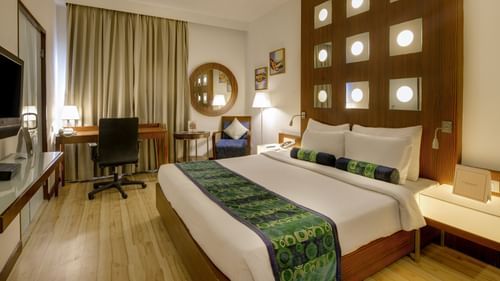 Superior Room at Pride Premier Chennai featuring a plush bed with a fancy headboard and a work desk along with sitting space in the background