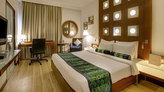 Superior Room at Pride Hotel Chennai featuring a plush bed with a fancy headboard and a work desk along with sitting space in the background