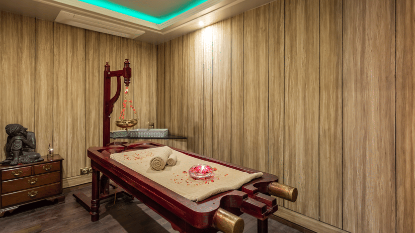 Luxurious spa treatment room with wood-paneled walls, ambient lighting, and a neatly arranged massage table, highlighting the tranquil wellness amenities at The Manor Sports & Wellness Hotel in Shimla.
