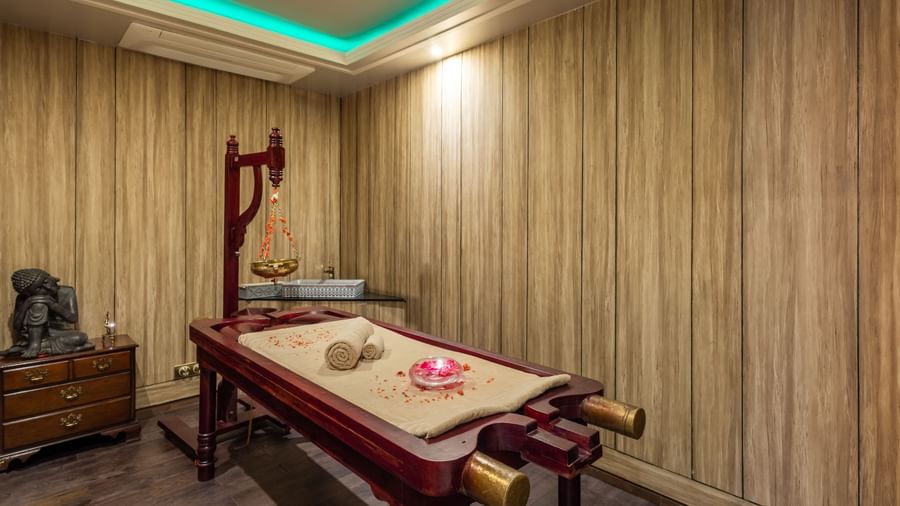 Luxurious spa treatment room with wood-paneled walls, ambient lighting, and a neatly arranged massage table, highlighting the tranquil wellness amenities at The Manor Sports & Wellness Hotel in Shimla.