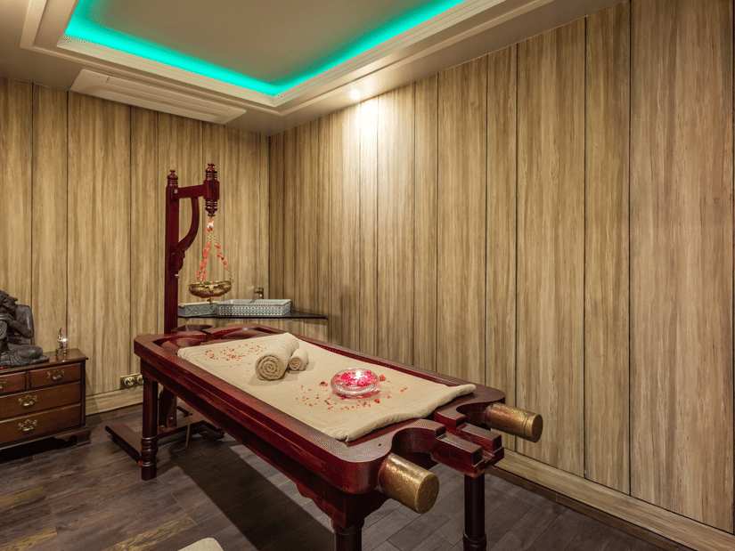 A luxurious spa treatment room with wood-panelled walls, ambient lighting, and a neatly arranged massage table, highlighting the tranquil wellness amenities at The Manor Sports & Wellness Hotel, a Hotels with a Spa in Shimla.