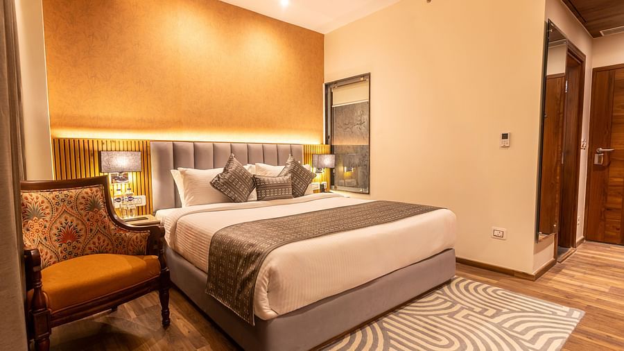 An image of a Deluxe room with bed, bed side table, lamps, chair, rug, and subtle lighting for decoration - The Belvedere Himalayan Retreat, McLeodganj