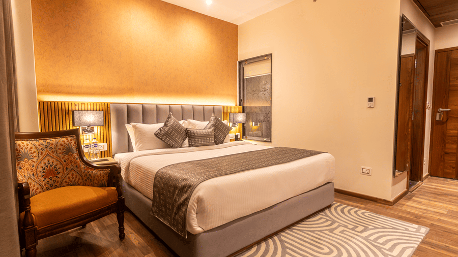 An image of a Deluxe room with bed, bed side table, lamps, chair, rug, and subtle lighting for decoration - The Belvedere Himalayan Retreat, McLeodganj
