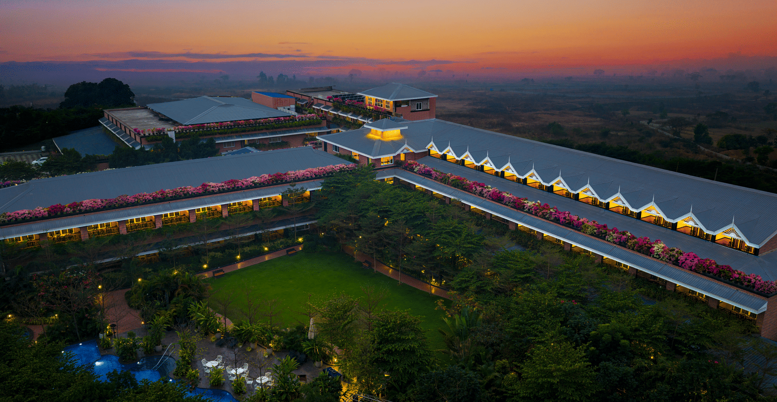 Aerial view of the sprawling layout of MAYFAIR Oasis Resort & Convention Jharsuguda with manicured lawn and lush greenery against a vibrant sunset sky.
