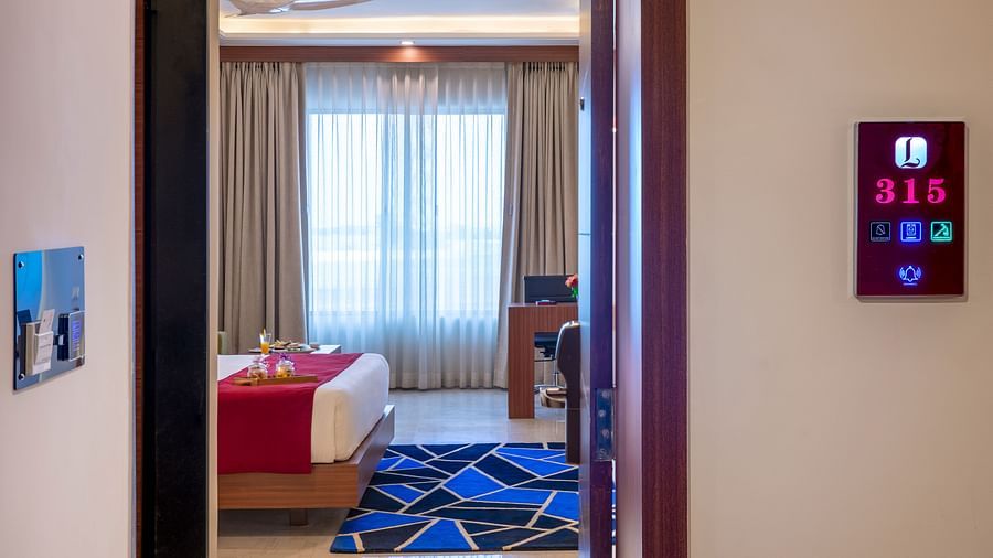 View from a doorway into a cozy bedroom with curtains drawn over tall windows - Lords Eco Inn Shapar Rajkot