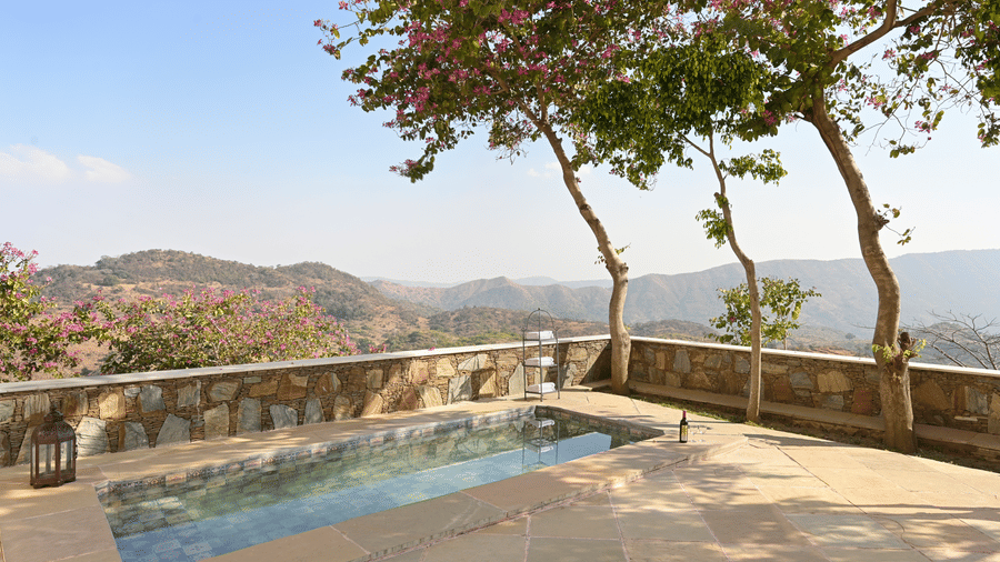 Outdoor view of Plunge Pool Suite at Fateh Safari Suites featuring a small pool surrounded by a few trees and a view of green hills from the balcony.