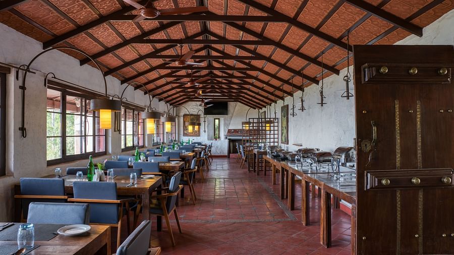 Wide view of a dining area with wooden tables and chairs, under a traditional wooden ceiling. | Mango Hill, Yercaud
