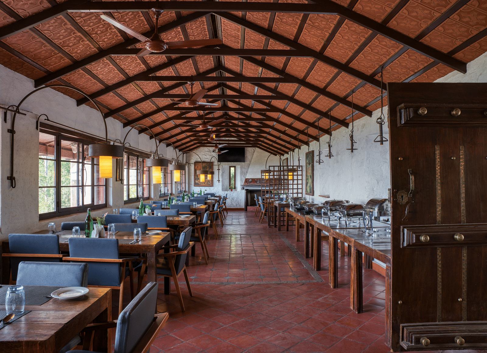 Wide view of a dining area with wooden tables and chairs, under a traditional wooden ceiling. | Mango Hill, Yercaud