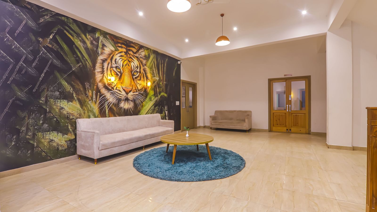 A spacious lobby at Vedikant Resorts The Mallard Corbett has sofas, a rug, and a wall with a tiger image.