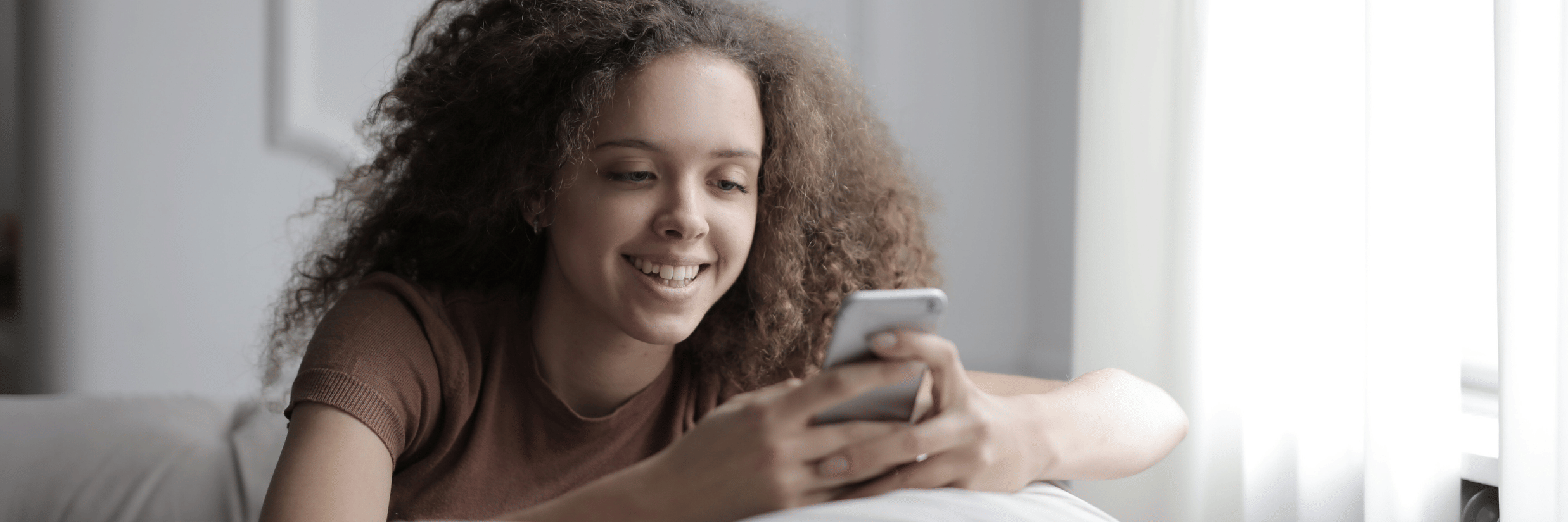 A close up of a woman sitting on a sofa while using her mobile phone.