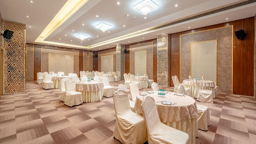 Spacious banquet hall with round tables and elegant chairs | Meetings & Events | Pravasa Hotel, Vijayapura
