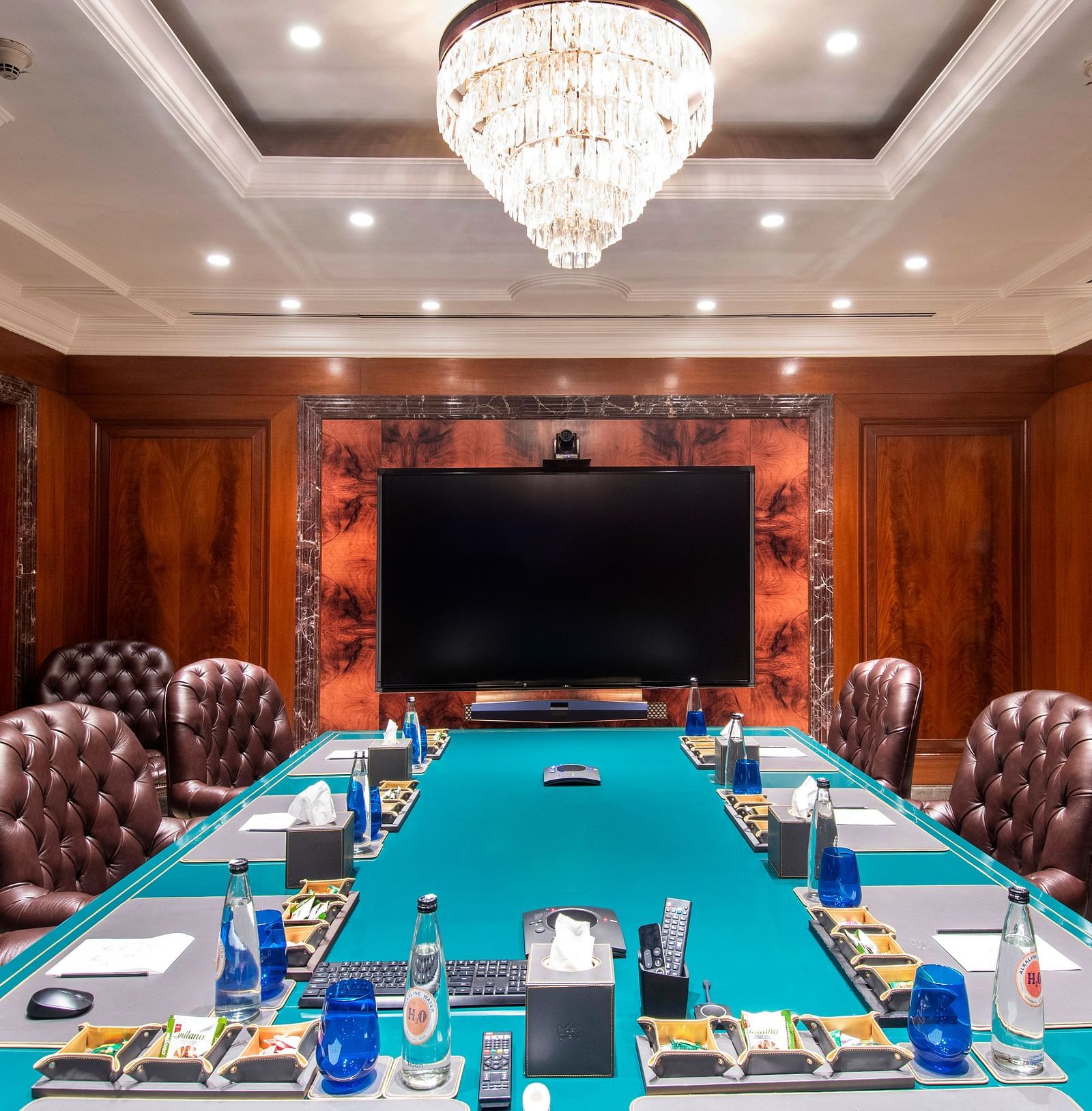 A luxurious boardroom with plush leather chairs, a large screen, and an elegant chandelier at The Claridges - Claridges Collection