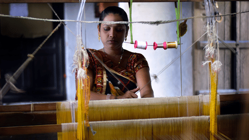 a woman weaving threads to make a garment using the traditional weaving techniques