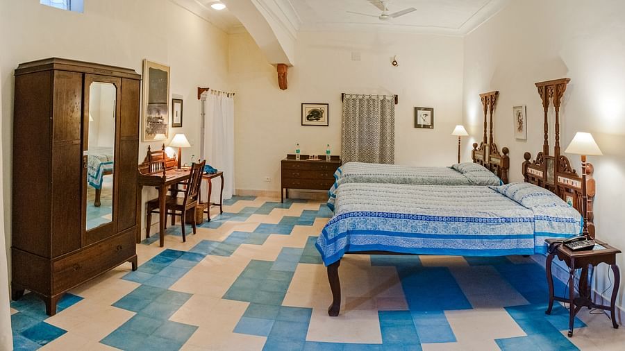 Spacious room with two beds, wooden wardrobe and desk, patterned floor, and lamps at Tijara Fort-Palace, Alwar.