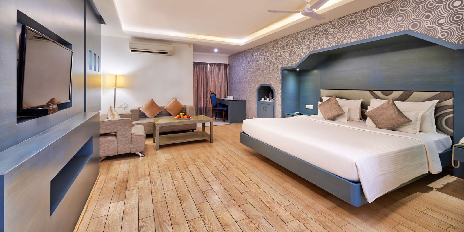 A modern hotel bedroom with a large bed, a sofa, a coffee table, and a wall-mounted television | Grande Chalet | Grand Bay Resort and Spa