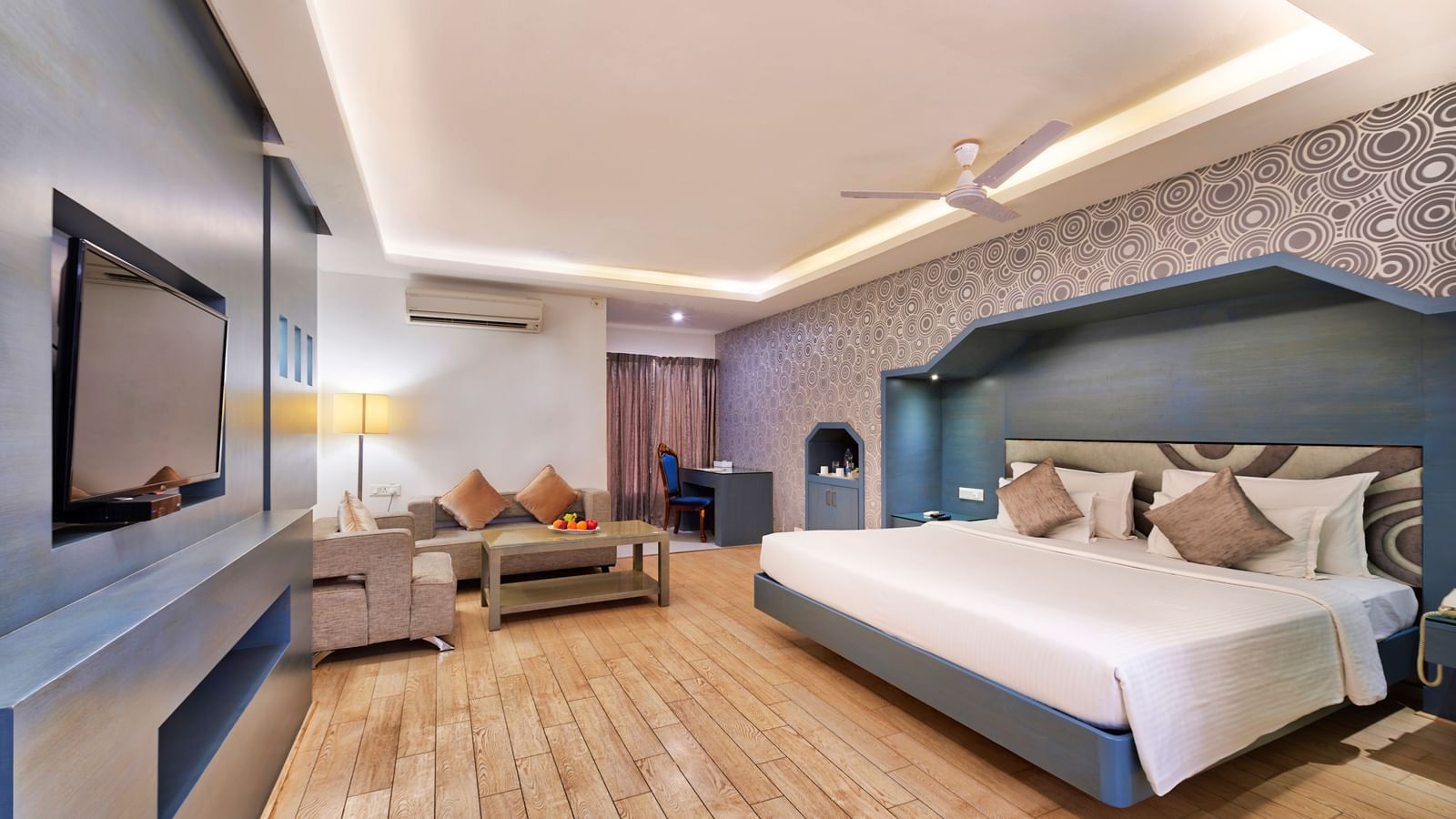 A modern hotel bedroom with a large bed, a sofa, a coffee table, and a wall-mounted television | Grande Chalet | Grand Bay Resort and Spa