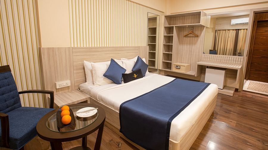 A side angle view of the Executive room at Hotel Bawa Regency, Dadar, featuring a comfy bed, a tea table, and a chair.