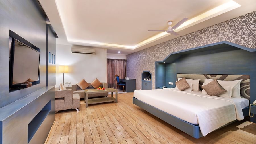 A modern hotel bedroom with a large bed, a sofa, a coffee table, and a wall-mounted television | Grande Chalet | Grand Bay Resort and Spa