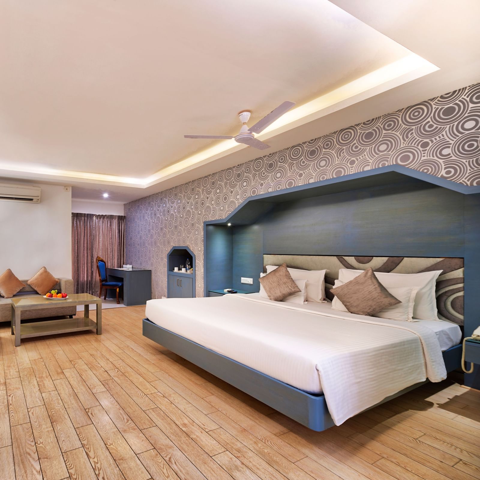 A modern hotel bedroom with a large bed, a sofa, a coffee table, and a wall-mounted television | Grande Chalet | Grand Bay Resort and Spa