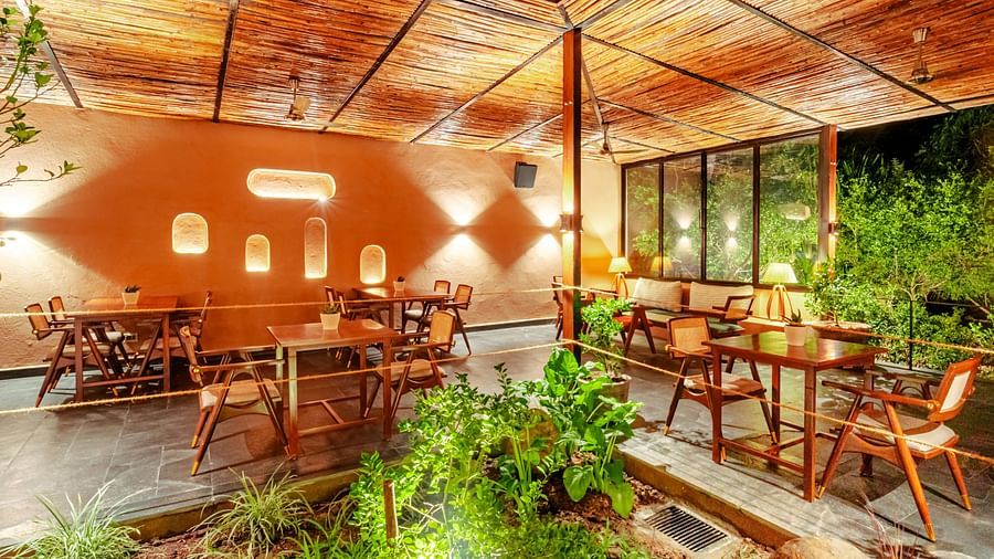 Interior view of a botanical bar, with short plants, wooden chairs and tables, and simple lighting in the photo.