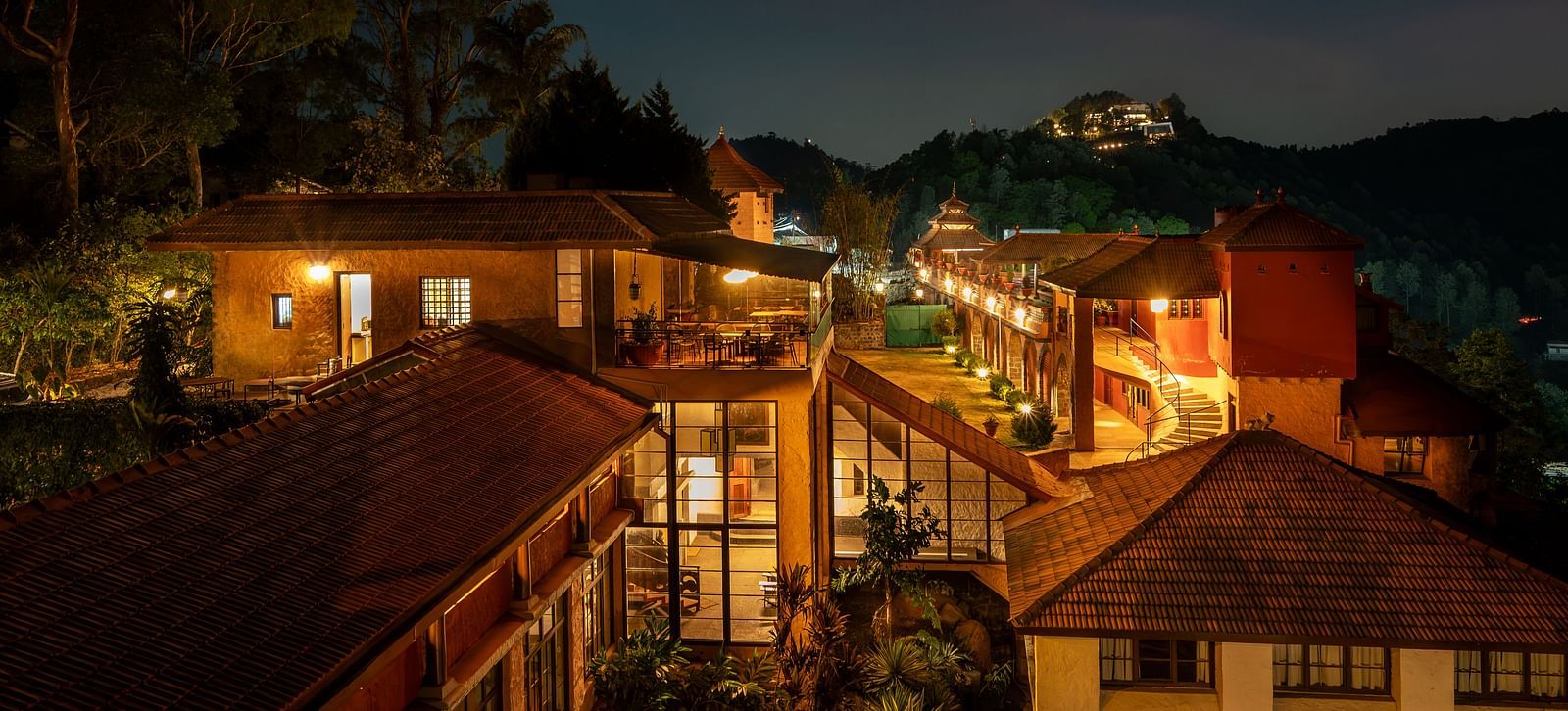 Night view of a resort with warmly lit pathways and buildings nestled in a hilly, forested landscape.  | Mango Hill, Yercaud