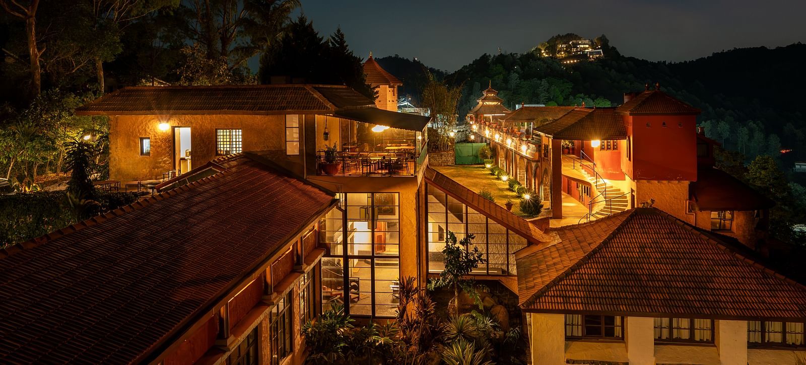 Night view of a resort with warmly lit pathways and buildings nestled in a hilly, forested landscape.  | Mango Hill, Yercaud