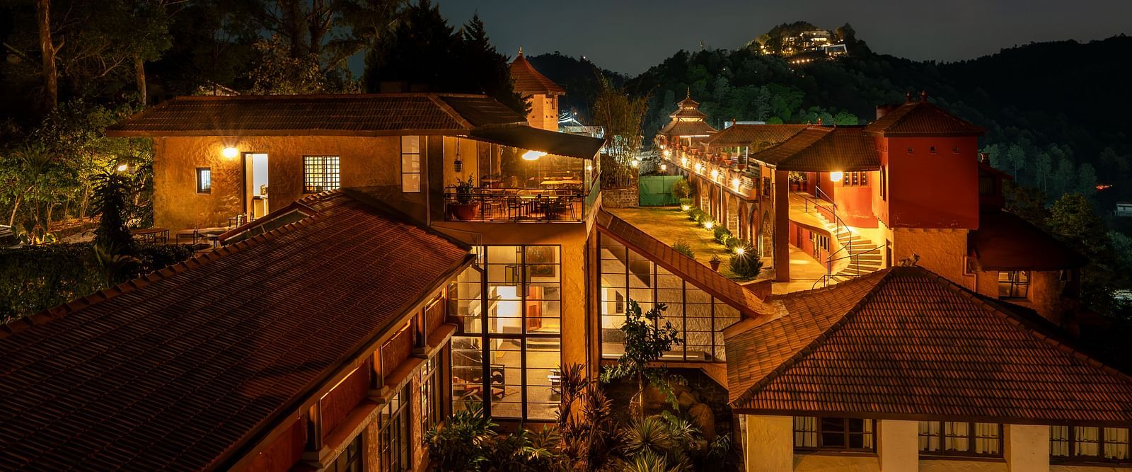 Night view of a resort with warmly lit pathways and buildings nestled in a hilly, forested landscape.  | Mango Hill, Yercaud