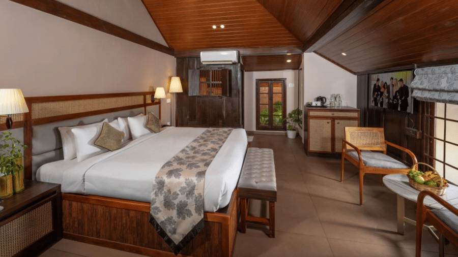 Lake View Heritage Room at Uday Backwater Resort featuring a king size bed, elegant wooden furnishings, sloped ceiling, seating area, and scenic lake views.