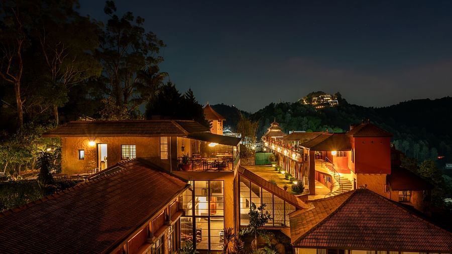 Night view of a resort with warmly lit pathways and buildings nestled in a hilly, forested landscape.  | Mango Hill, Yercaud