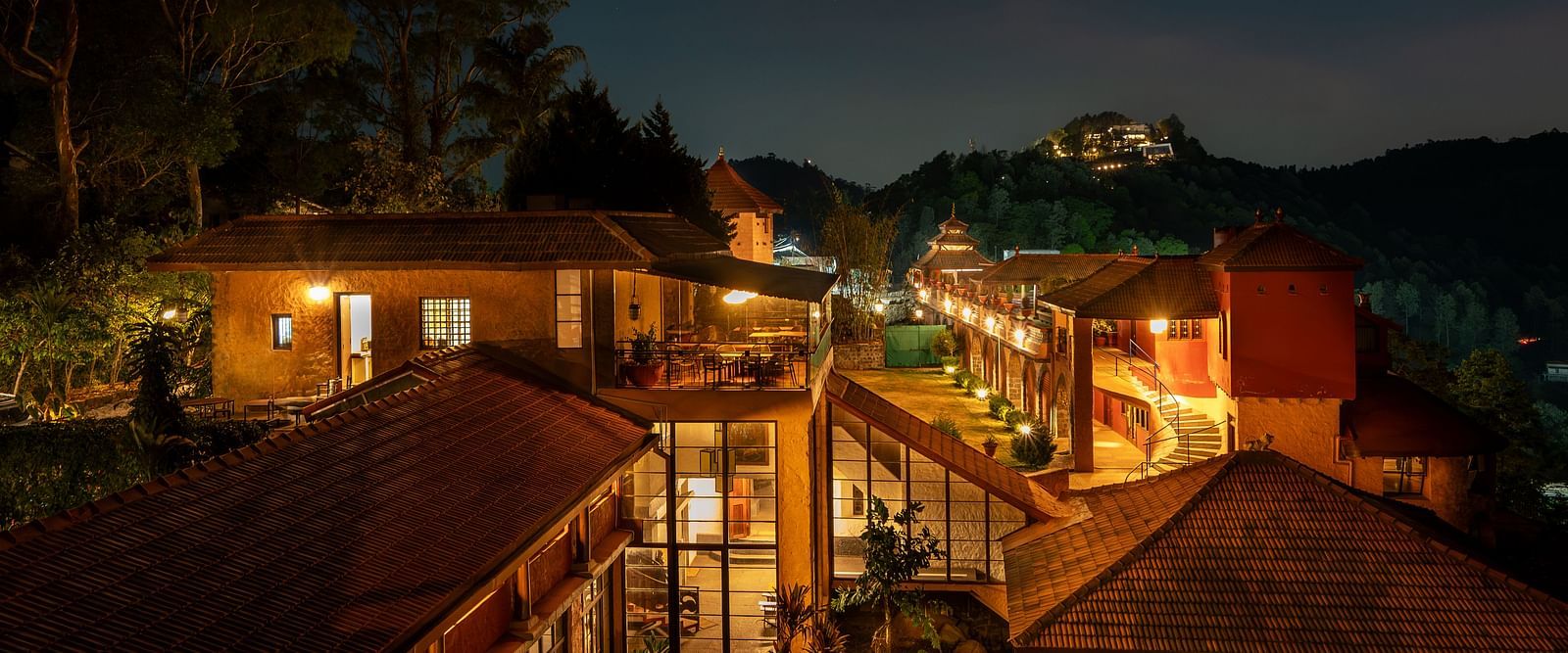 Night view of a resort with warmly lit pathways and buildings nestled in a hilly, forested landscape.  | Mango Hill, Yercaud
